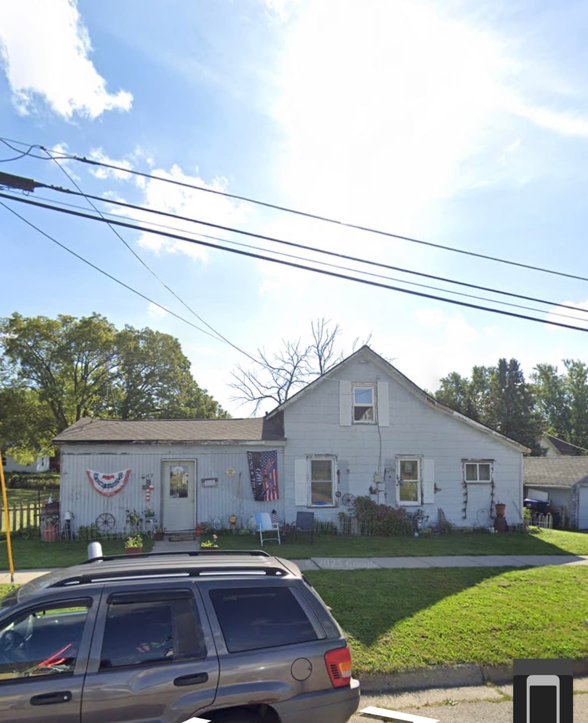 Small light blue house with American flags and a grey SUV parked in the foreground.